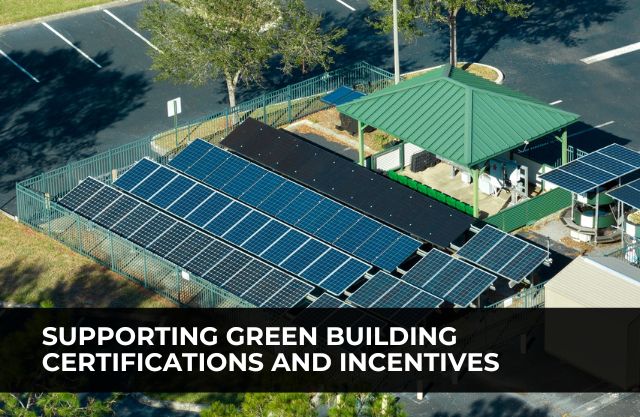 A small-scale solar installation beside a green-roofed utility building, surrounded by fencing in a commercial parking area. The solar panels represent efforts to achieve green building certifications and take advantage of sustainability incentives.